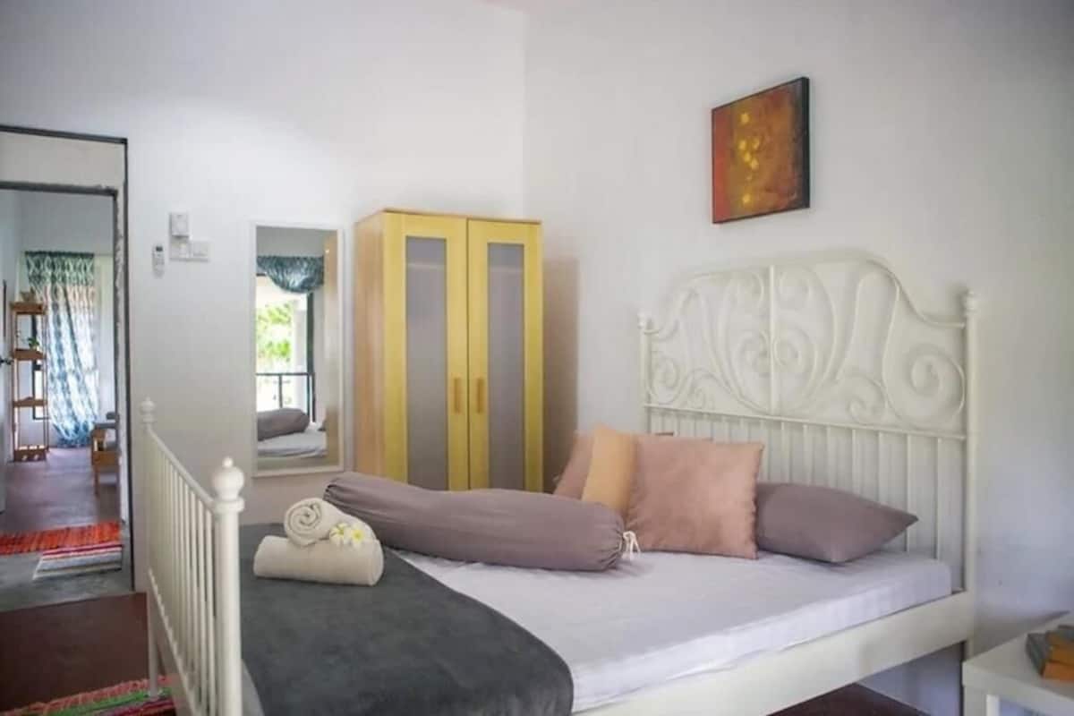 Quarto com cama branca, guarda-roupa amarelo e um quadro na parede.