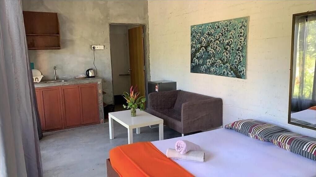 Una habitación con cama, sofá, una mesita, zona de cocina y un cuadro en la pared.