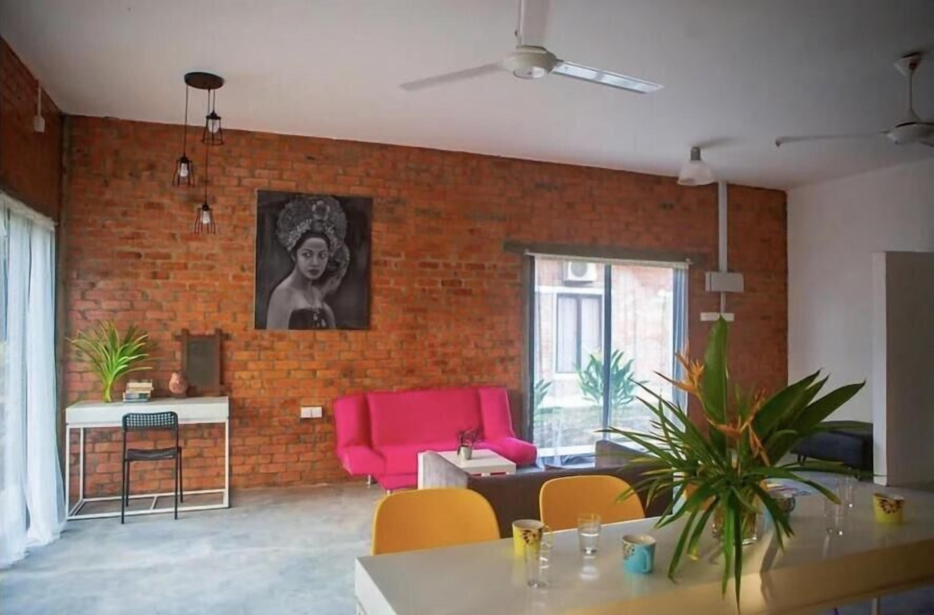 A dining area with a brick wall, a pink sofa, a dining table with chairs, and a ceiling fan.