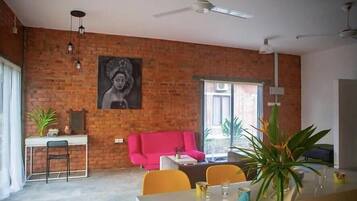 A dining area with a brick wall, a pink sofa, a dining table with chairs, and a ceiling fan.