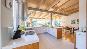 Une cuisine moderne avec des poutres en bois, des meubles blancs et une grande fenêtre donnant sur un jardin.