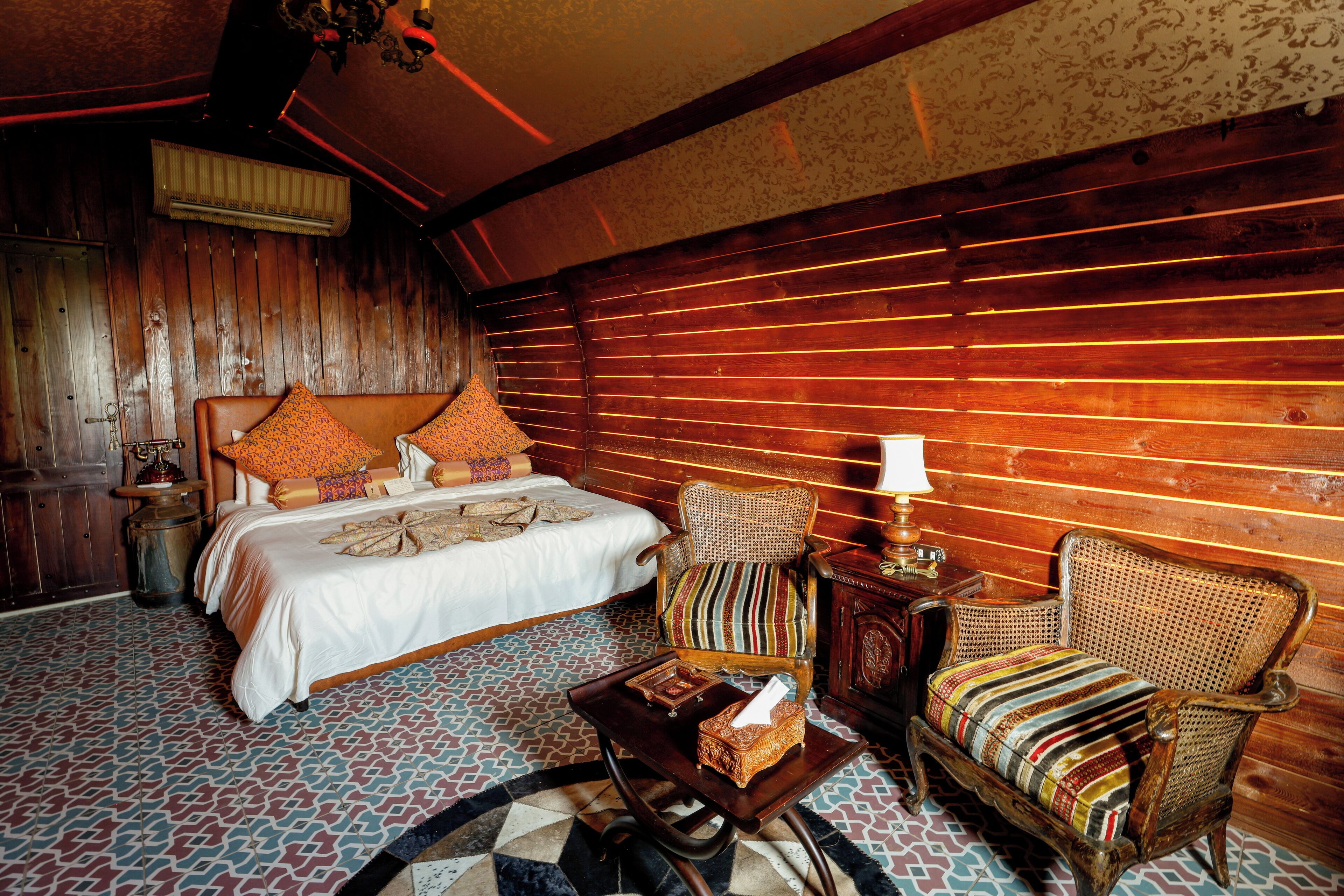 A room with a bed, two chairs, a small table, and a patterned floor.