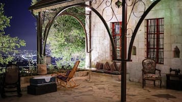 A covered outdoor seating area with stone flooring, a wooden bench, and a wicker chair.