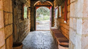 A stone corridor with a wooden bench, a hanging light fixture, and a view of the outside. - Chateau Du Comte (Daraaoun)