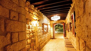 A stone-walled corridor with a tiled floor, wooden benches, and a hanging light fixture. - Chateau Du Comte (Daraaoun)
