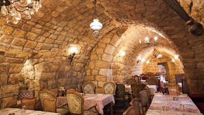 An underground dining area with stone walls, wooden tables, and chairs. - Chateau Du Comte (Daraaoun)