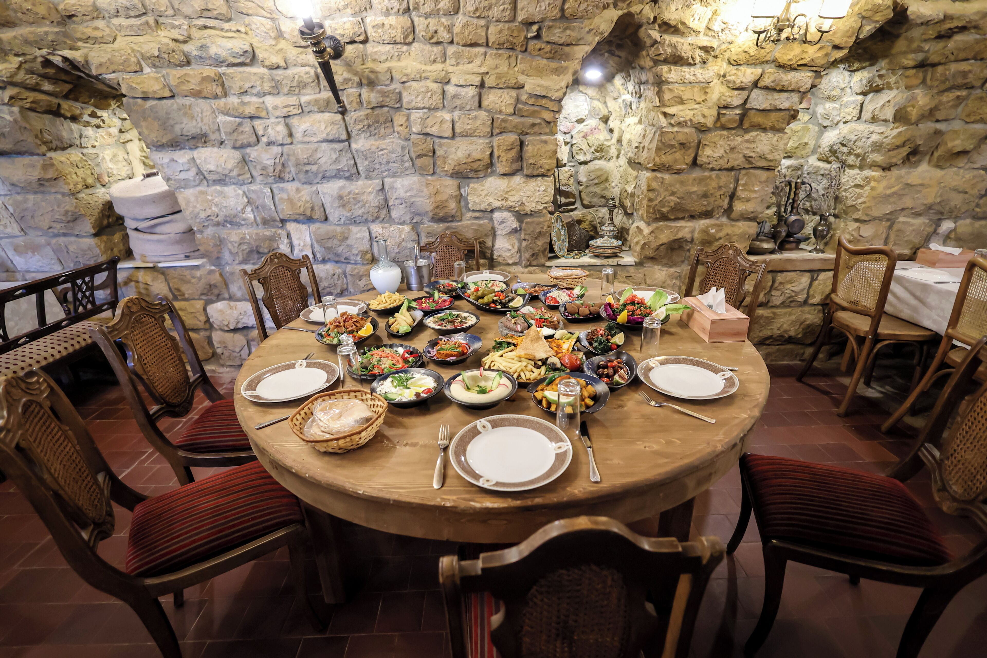 A stone-walled dining area with a round table set for a meal, surrounded by wicker chairs.