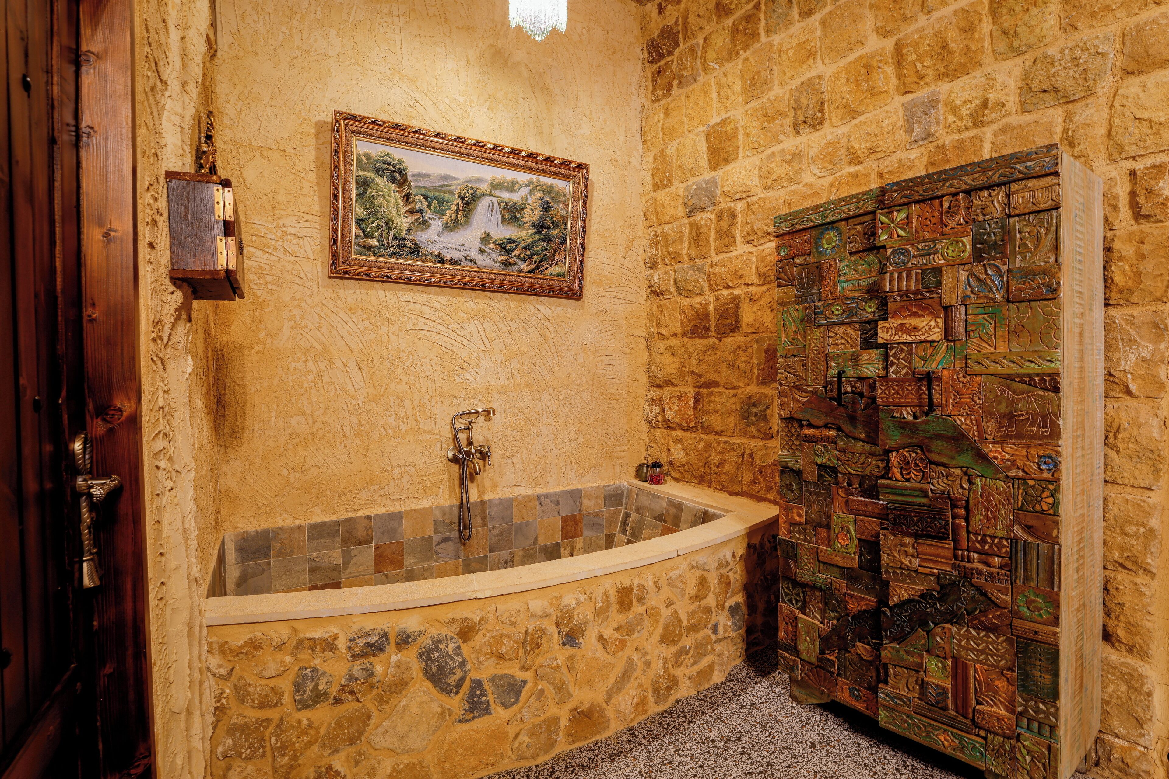 Une salle de bain aux murs en pierre, dotée d’une baignoire sur pieds, d’un tableau représentant un paysage encadré et d’un panneau décoratif en bois.
