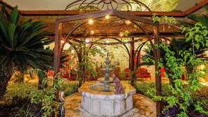 A covered garden area with a central fountain, surrounded by lush greenery and a brick wall. - Chateau Du Comte (Daraaoun)