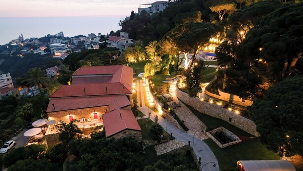 A hillside property with a red-roofed building, stone walls, and a well-lit garden area. - Chateau Du Comte (Daraaoun)