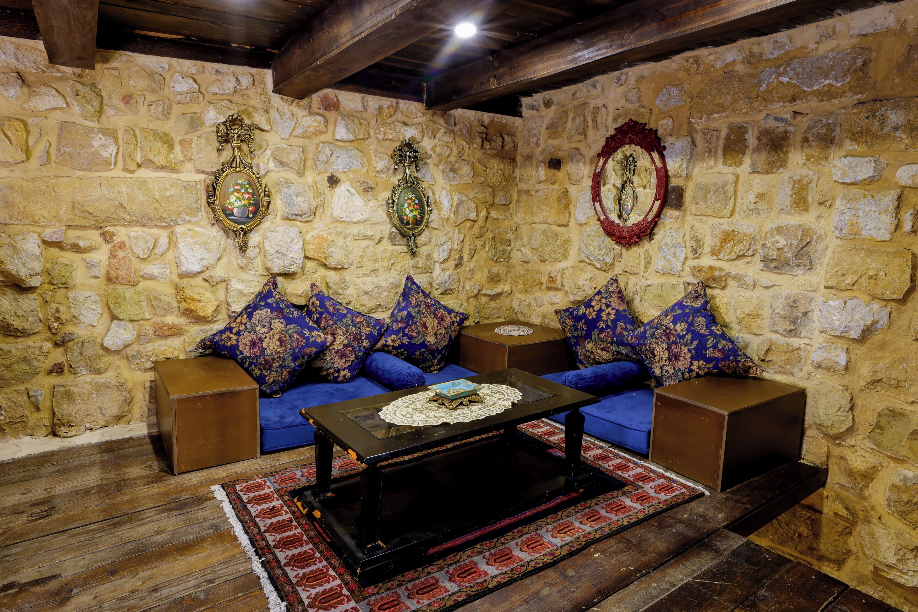 A stone-walled room with a blue sofa set, a wooden coffee table, and decorative wall mirrors.
