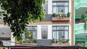 Un edificio moderno con entrada protegida, balcones con plantas y un cartel visible.