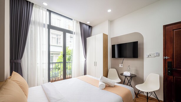 Habitación de hotel con cama, televisor montado en la pared, una mesita con una botella y una silla.