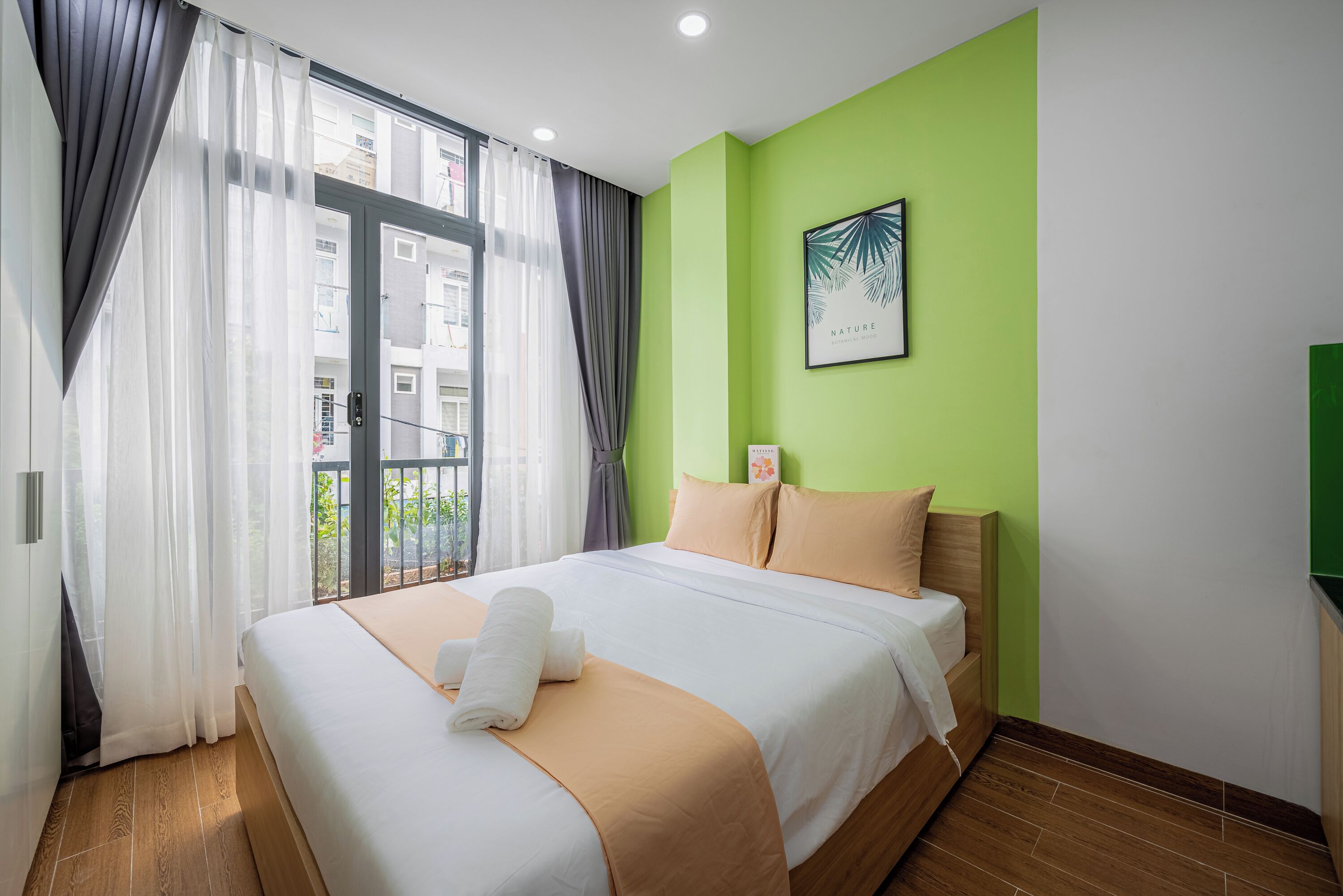 Quarto de hotel com cama, paredes verdes, janela com cortinas e um quadro na parede.