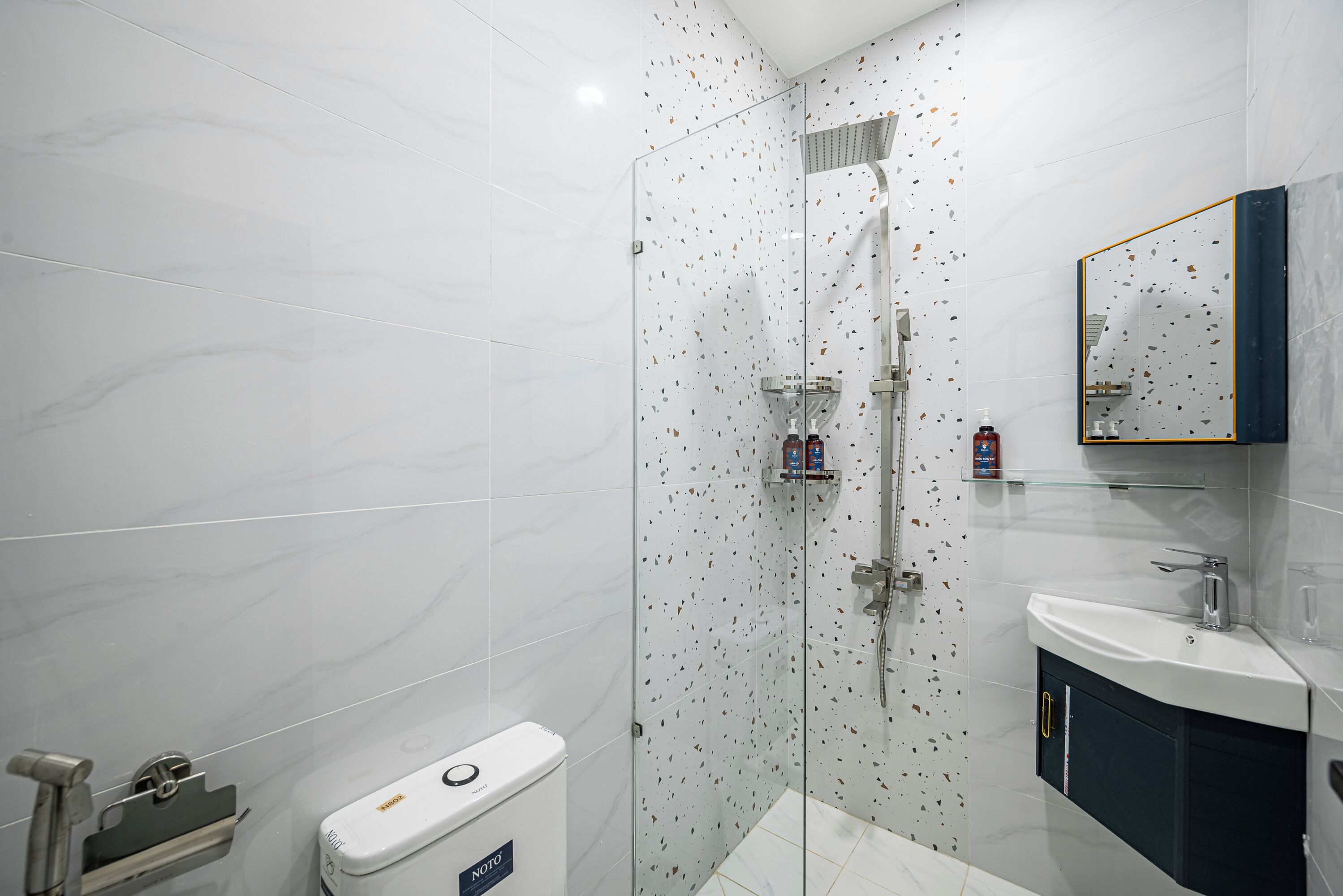 A modern bathroom with a glass-enclosed shower, a white toilet, and a sink with a mirror above it.