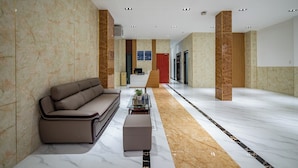 Un moderno hall de entrada con un sofá, reposapiés y una mesa de vidrio.