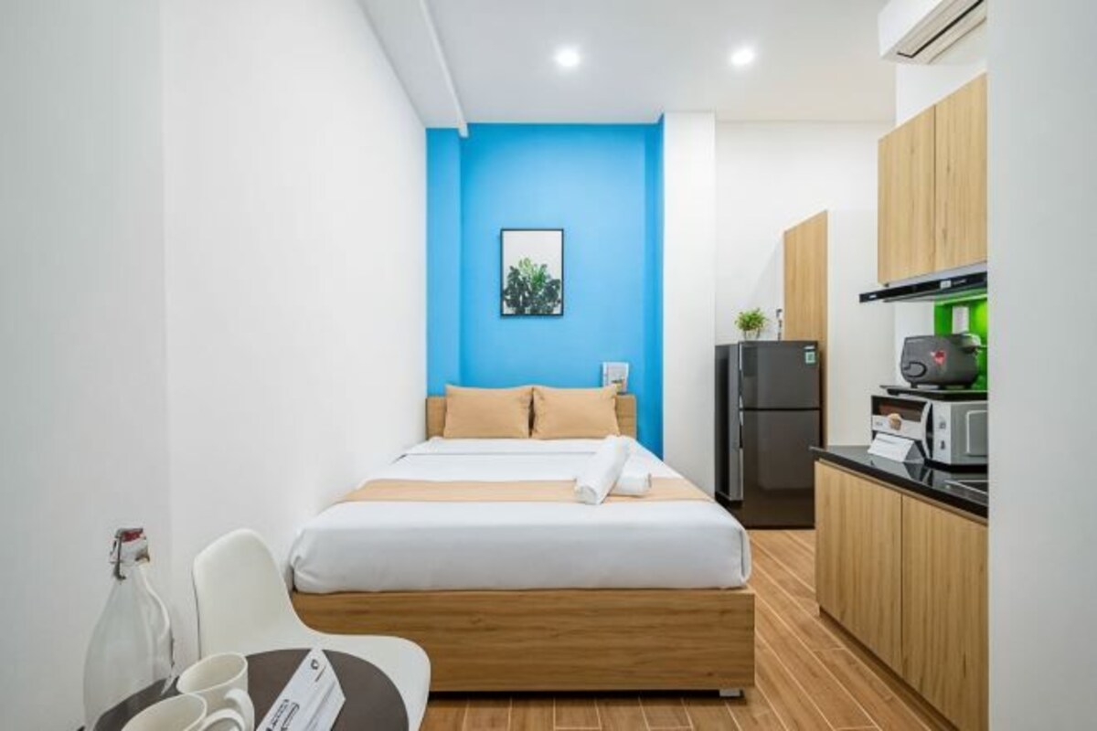 A compact hotel room with a bed, a small kitchenette, and a chair.