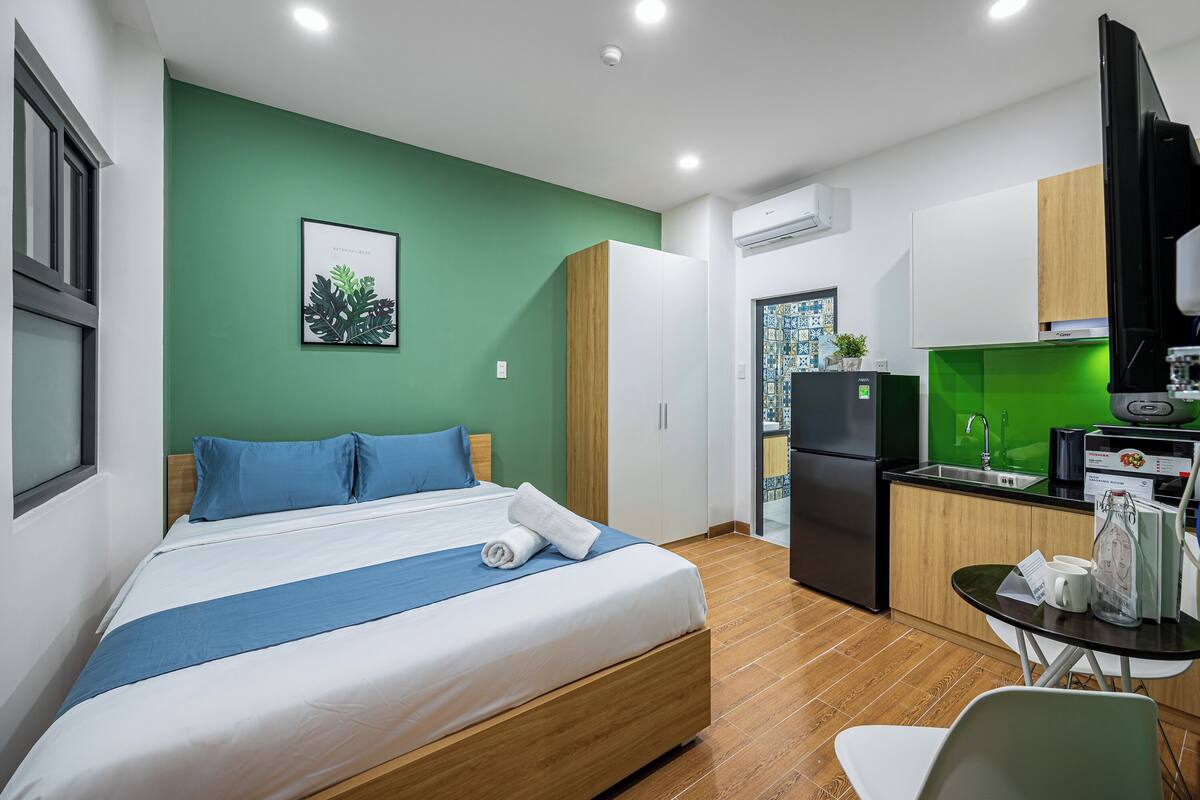 Una habitación de hotel moderna con una cama, un pequeño espacio de cocina y una mesa de comedor.