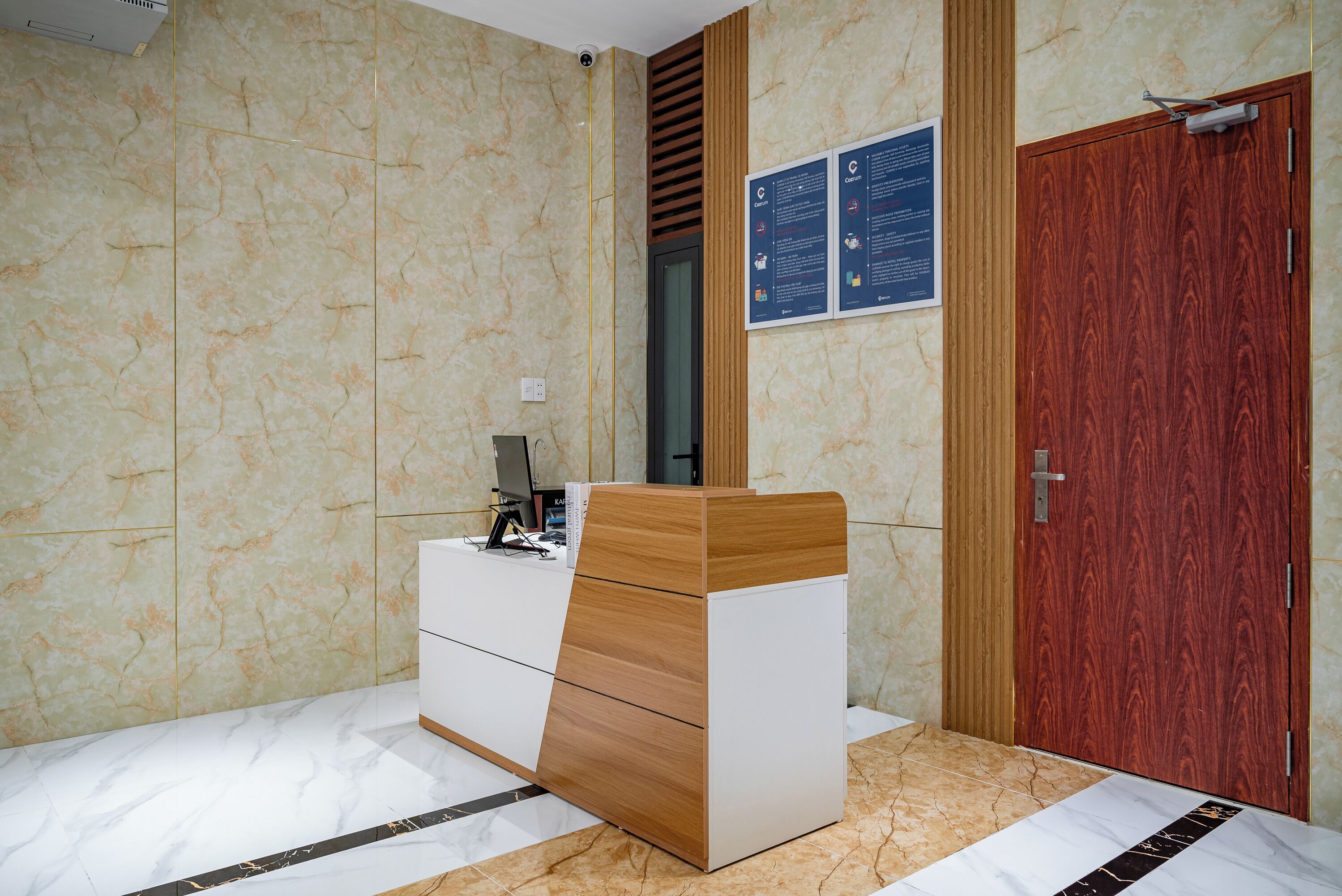 Habitación de hotel con pared de diseño de mármol, un armario de madera, una puerta de madera y un tablón de anuncios con información.