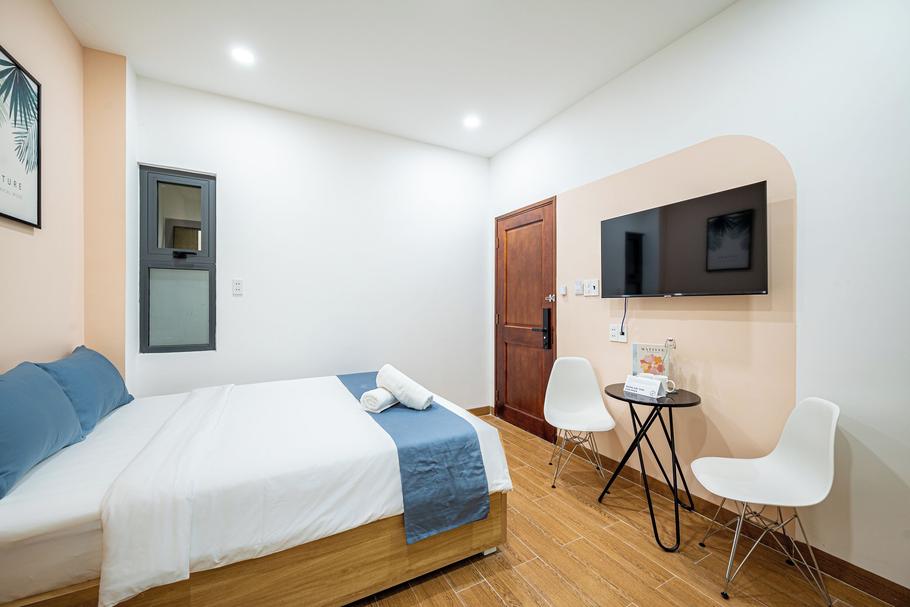 A neatly arranged hotel room with a bed, a TV mounted on the wall, a small table with a chair, and a door.