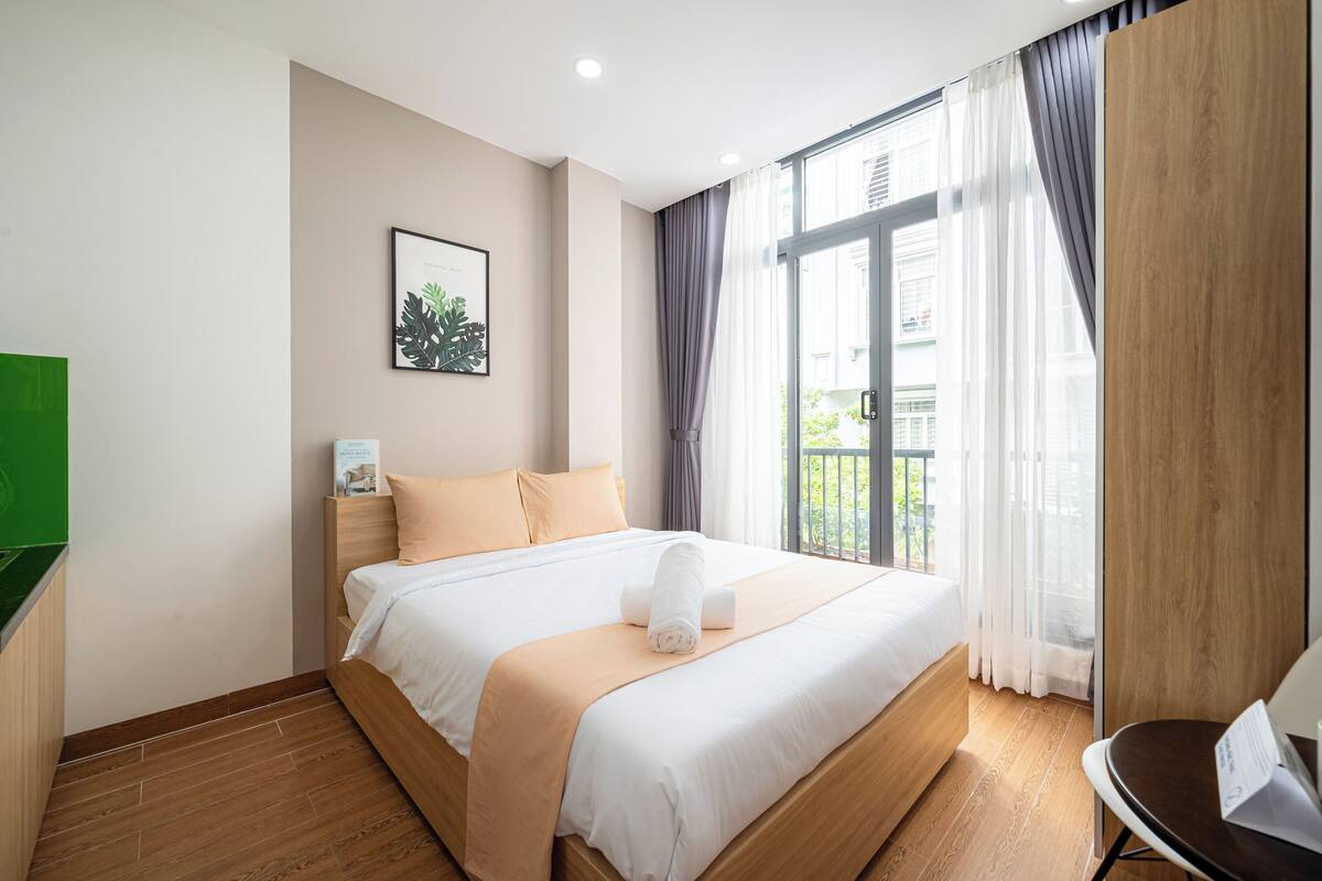 Una habitación de hotel con cama, mesita de noche, un cuadro enmarcado y una ventana con cortinas.