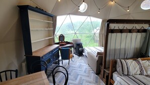 Um quarto aconchegante com uma escrivaninha de madeira, uma cama com roupa de cama listrada e uma grande janela com vista para o verde.