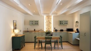 A modern kitchen with light green cabinets, a wooden dining table with four chairs, and a central island with a built-in stove. - Clairette- Charming gîte, 2 bedrooms (Gonfaron)
