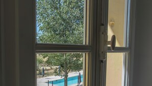 A window view of a swimming pool area with a tree, a fence, and a clear sky. - Clairette- Charming gîte, 2 bedrooms (Gonfaron)