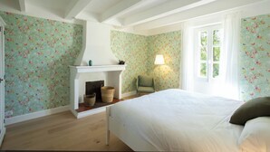 A bedroom with floral wallpaper, a fireplace, a bed, and a window. - Clairette- Charming gîte, 2 bedrooms (Gonfaron)