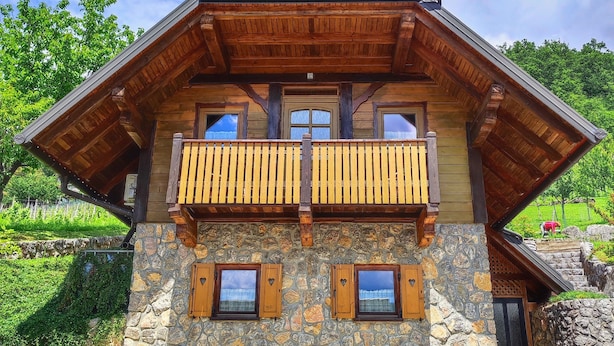 A two-story wooden house with a stone facade, a balcony with wooden railings, and a stone wall in front. - Vineyard cottage Kralj (Dolenjske Toplice)