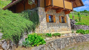 A two-story wooden house with a stone facade, a balcony, and a stone retaining wall. - Vineyard cottage Kralj (Dolenjske Toplice)
