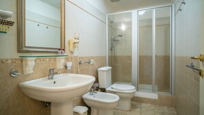 Een badkamer met een wastafel, twee toiletten, een douche en een douchegedeelte met glazen wanden.