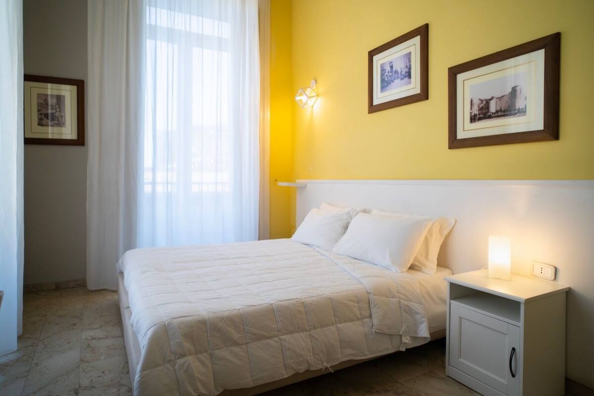A hotel room with a bed, a nightstand, and two framed pictures on the wall.