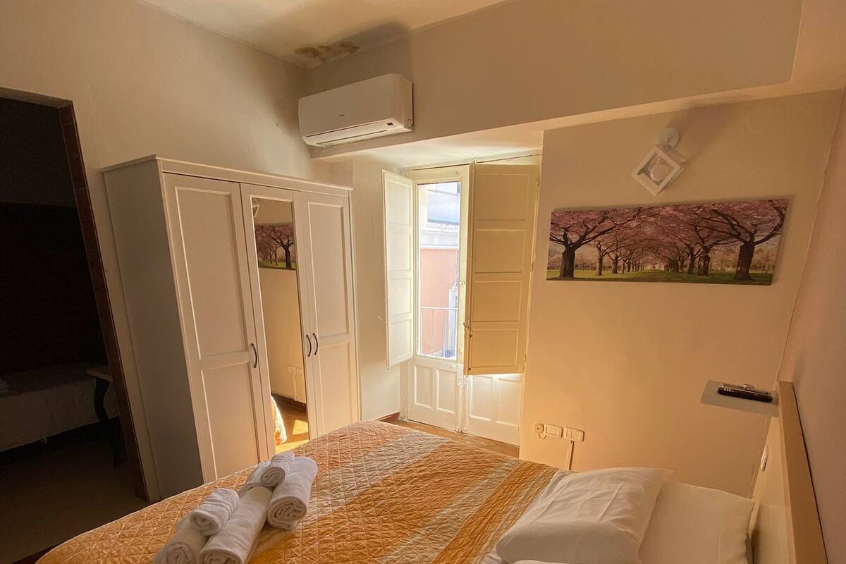 A hotel room with a bed, a wardrobe, a painting, and an air conditioning unit.