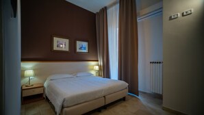 Een hotelkamer met een bed, twee bedlampen, een radiator en twee ingelijste foto's aan de muur.