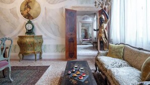 Une pièce au décor d’époque, avec un canapé, une table basse sur laquelle sont disposées des pâtisseries, une horloge et une statue.
