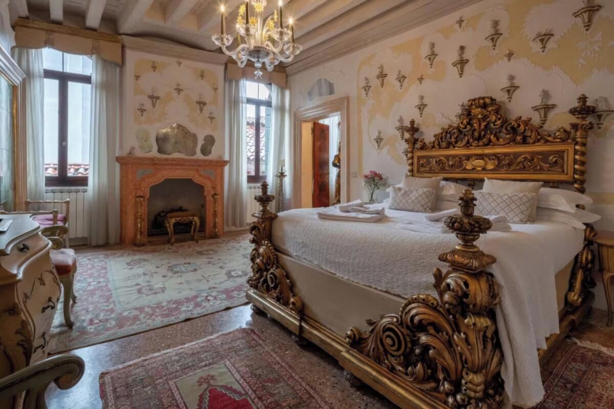 A luxurious bedroom with an ornate bed, a fireplace, and a chandelier.