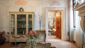 Une pièce au décor d’époque, avec un meuble, un vase de fleurs et une porte donnant sur une autre pièce.