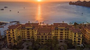 Un hotel frente al mar con varios balcones, un puerto deportivo con barcos y vistas al atardecer.