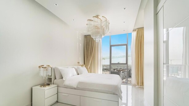 Ein modernes Schlafzimmer mit einem großen Bett, einem Nachttisch, einer Kronleuchter und Blick auf die Stadt.
