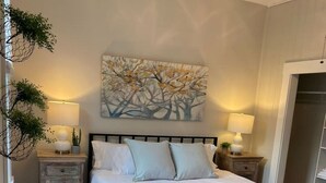 Ein Schlafzimmer mit einem Bett, zwei Nachttischen, einem Wandbild und einer Stehlampe.