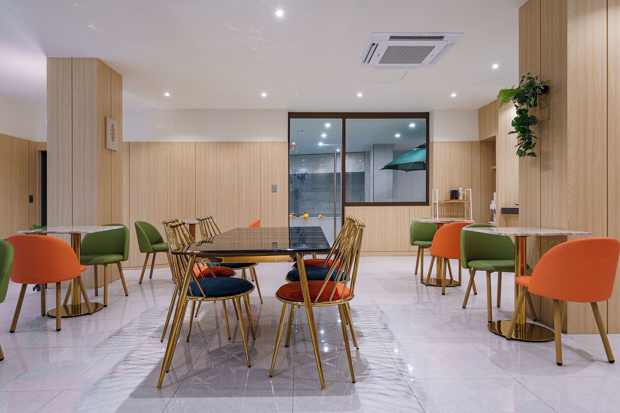 Una sala de reuniones moderna con una mesa de vidrio, sillas verdes y anaranjadas, y un ventanal con vistas.