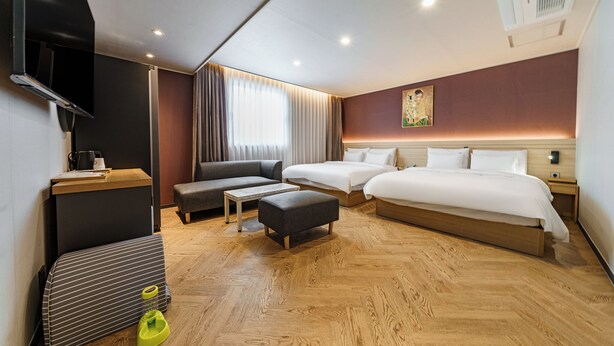 A modern hotel room with a wooden floor, a sofa, two single beds, a small table, and a TV. - Browndot Samcheonpo (Sacheon)