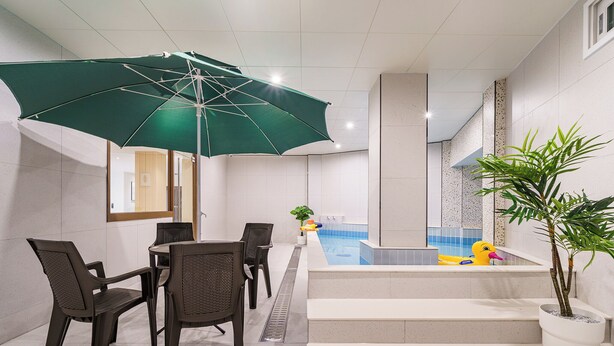 A pool area with a table and chairs, a green umbrella, and a small duck float. - Browndot Samcheonpo (Sacheon)