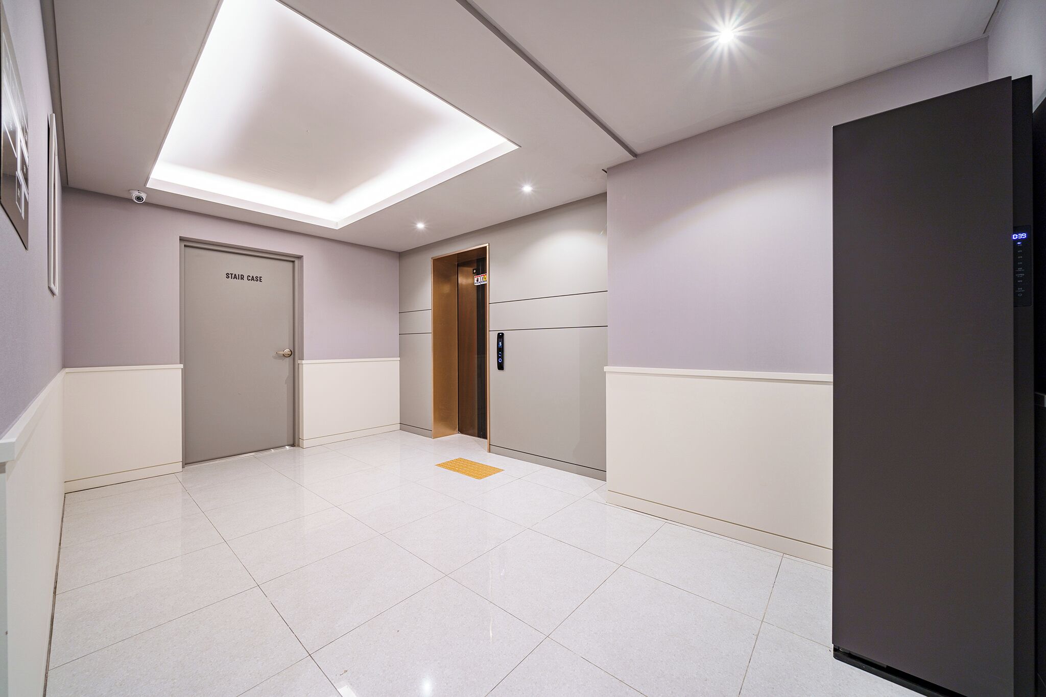 Un couloir moderne avec un escalier, une porte et un réfrigérateur.