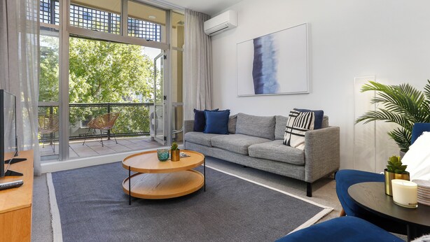 Un salon moderne avec un canapé gris, une table basse ronde en bois et une grande fenêtre donnant sur la forêt.