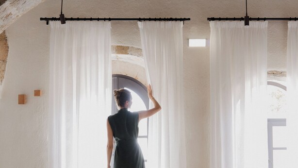 Une pièce dotée d’un plafond voûté, d’un lit recouvert d’un tapis aux couleurs vives et d’une fenêtre ornée de rideaux blancs.
