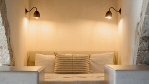 Une chambre à coucher avec un lit, deux lampes fixées au mur et un mur en pierre.
