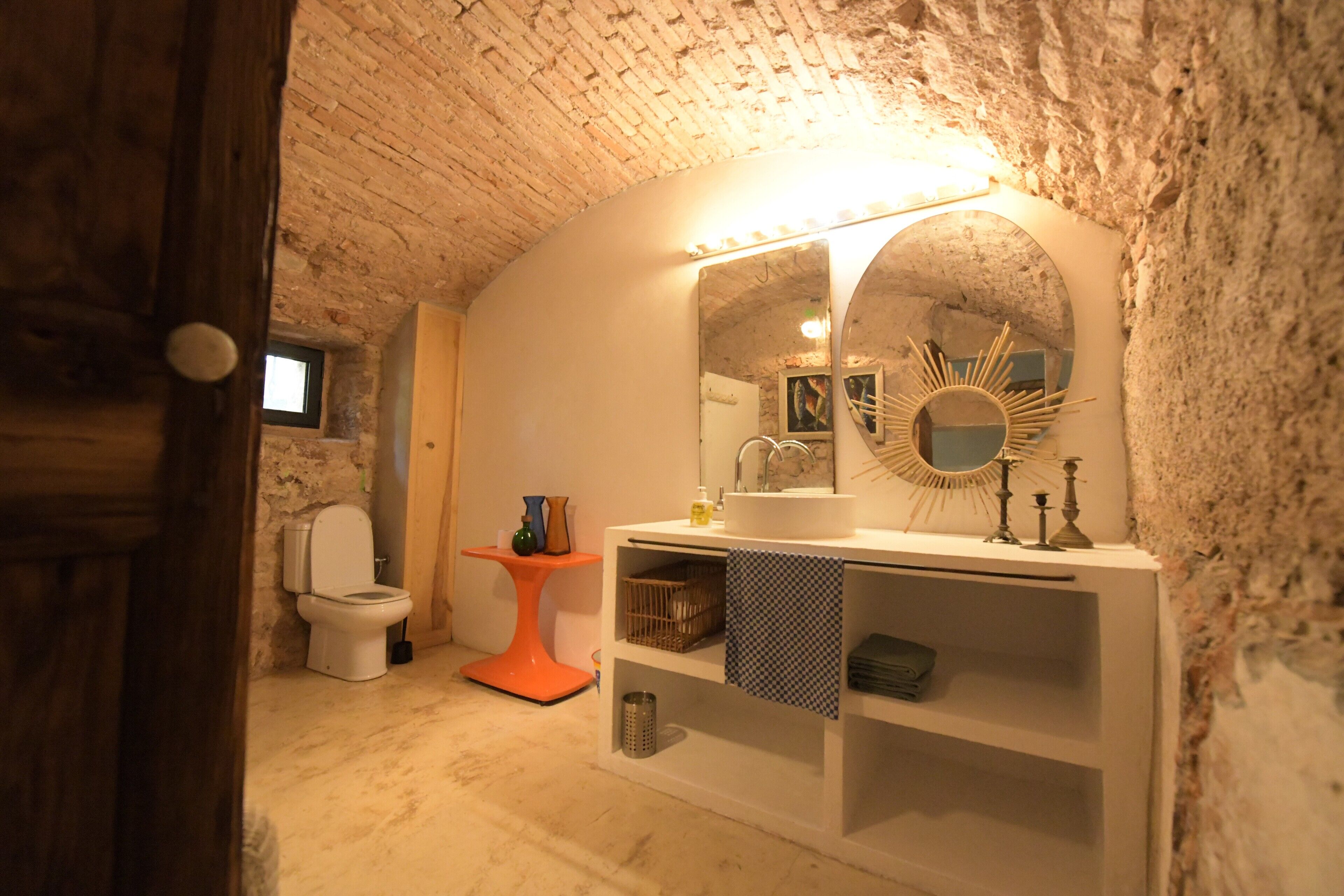 A rustic bathroom with a white sink, mirror, and orange pedestal table.