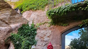 A courtyard with potted plants, a red gnome statue, and a building with ivy-covered walls and a wooden balcony. - Historic Catalan country house located in a natural park and 40' from Barcelona! (Sant Llorenç Savall)